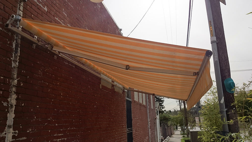 red brick wall with an orange stripe slide on wire retractable awning - custom awnings - custom aluminum awnings - custom awning designs - custom awnings cost - retractable awnings - spear awnings - convex awnings - patio shades