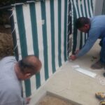 two men installing a stripe privacy panel - custom awnings - custom awnings near me - custom awnings for decks - custom awnings for business - custom door awnings near me - spear awnings - aluminum awnings - dome awnings