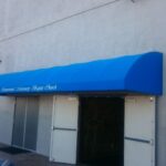 grey building with blue entrance canopy - custom awnings - custom awnings near me - custom awnings for decks - custom awnings for business - custom door awnings near me - spear awnings - aluminum awnings - dome awnings
