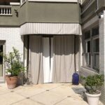a green house with a privacy panel and plant on the entrance - custom awnings - custom awnings near me - custom awnings for decks - custom awnings for business - custom door awnings near me - spear awnings - aluminum awnings - dome awnings