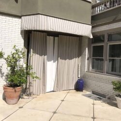 a green house with a privacy panel and plant on the entrance - custom awnings - custom awnings near me - custom awnings for decks - custom awnings for business - custom door awnings near me - spear awnings - aluminum awnings - dome awnings