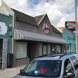restaurant with stripe awnings with a car passing by - custom awnings - custom awnings near me - custom awnings for decks - custom awnings for business - custom door awnings near me - spear awnings - aluminum awnings - dome awnings
