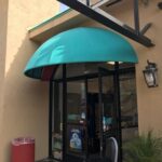 yellow store with green dome awnings and plants in front - custom awnings - custom awnings near me - custom awnings for decks - custom awnings for business - custom door awnings near me - spear awnings - aluminum awnings - dome awnings