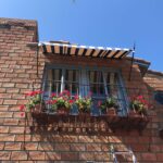 brick building with stripe spear awning for a small balcony with plants - custom awnings - custom awnings near me - custom awnings for decks - custom awnings for business - custom door awnings near me - spear awnings - aluminum awnings - dome awnings
