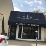 Carlton Drew with storefront awning and a car parked in front - custom awnings - custom awnings near me - custom awnings for decks - custom awnings for business - custom door awnings near me - spear awnings - aluminum awnings - dome awnings