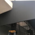 two men installing a black awning for a store - custom awnings - custom awnings near me - custom awnings for decks - custom awnings for business - custom door awnings near me - spear awnings - aluminum awnings - dome awnings
