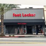 two men installing a black awning for a foot locker store - custom awnings - custom awnings near me - custom awnings for decks - custom awnings for business - custom door awnings near me - spear awnings - aluminum awnings - dome awnings