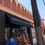 two men installing black storefront awnings - concave awnings - aluminum awnings - carports - store front awnings - patio shades