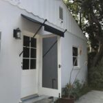a white house with a black spear awning for its white door - custom awnings - custom awnings near me - custom awnings for decks - custom awnings for business - custom door awnings near me - spear awnings - aluminum awnings - dome awnings