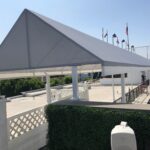 two men installing grey entrance canopy for a white building with flags in the background - custom awnings - custom awnings near me - custom awnings for decks - custom awnings for business - custom door awnings near me - spear awnings - aluminum awnings - dome awnings
