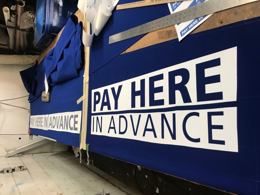 "pay here in advance" sign laid on a table - custom awnings - custom awnings near me - custom awnings for decks - custom awnings for business - custom door awnings near me - spear awnings - aluminum awnings - dome awnings