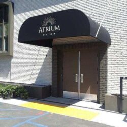 white brick building with black round awning for its entrance - custom awnings - custom awnings near me - custom awnings for decks - custom awnings for business - custom door awnings near me - spear awnings - aluminum awnings - dome awnings