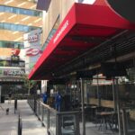 orange building with different restaurants with red awning for its entrance - custom awnings - custom awnings near me - custom awnings for decks - custom awnings for business - custom door awnings near me - spear awnings - aluminum awnings - dome awnings