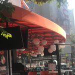 orange awnings for a restaurant with ball shaped lights hanging - concave awnings - aluminum awnings - carports - store front awnings - patio shades