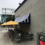 grey brick building with awnings for outdoor seating - custom awnings - custom awnings near me - custom awnings for decks - custom awnings for business - custom door awnings near me - spear awnings - aluminum awnings - dome awnings