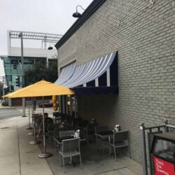 grey brick building with awnings for outdoor seating - custom awnings - custom awnings near me - custom awnings for decks - custom awnings for business - custom door awnings near me - spear awnings - aluminum awnings - dome awnings