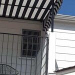 white house with a stripe awning for its balcony - custom awnings - custom awnings near me - custom awnings for decks - custom awnings for business - custom door awnings near me - spear awnings - aluminum awnings - dome awnings