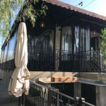 house with brown awnings and drapes for its second floor balcony - custom awnings - custom awnings near me - custom awnings for decks - custom awnings for business - custom door awnings near me - spear awnings - aluminum awnings - dome awnings
