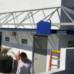 blue awnings being installed on a white building - custom awnings - custom awnings near me - custom awnings for decks - custom awnings for business - custom door awnings near me - spear awnings - aluminum awnings - dome awnings