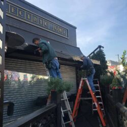 two men installing a black awning for a store - custom awnings - custom awnings near me - custom awnings for decks - custom awnings for business - custom door awnings near me - spear awnings - aluminum awnings - dome awnings