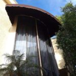large window with plants outside and a brown awning - custom awnings - custom awnings near me - custom awnings for decks - custom awnings for business - custom door awnings near me - spear awnings - aluminum awnings - dome awnings