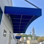 blue awnings for a white building with cars and truck in the background - custom awnings - custom awnings near me - custom awnings for decks - custom awnings for business - custom door awnings near me - spear awnings - aluminum awnings - dome awnings