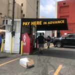 black awnings with text saying "pay here in advance" for a payment booth with two people using the ATM machine - custom awnings - commercial awnings - restaurant awnings - convex awnings - concave awnings - window awnings for shade - awning companies near me