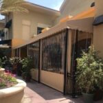 light brown awnings with drapes for a yellow home - custom awnings - custom awnings near me - custom awnings for decks - custom awnings for business - custom door awnings near me - spear awnings - aluminum awnings - dome awnings