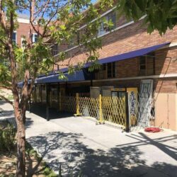 brick building with blue awning and trees in front - custom awnings - custom awnings near me - custom awnings for decks - custom awnings for business - custom door awnings near me - spear awnings - aluminum awnings - dome awnings