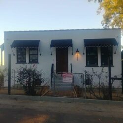 white house with gate and plants and awning for door and windows - custom awnings - custom awnings near me - custom awnings for decks - custom awnings for business - custom door awnings near me - spear awnings - aluminum awnings - dome awnings
