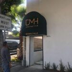 a man wearing a gray sweater and pants staring at the entrance of DMH aesthetics in Beverly Hills with round green awnings - round awnings - round door awnings - half round awnings - dome style window awning - dome door awnings - dome awnings for sale - retractable awnings