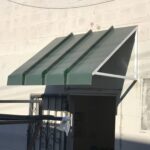 dirty white building with green aluminum awning - custom awnings - custom awnings near me - custom awnings for decks - custom awnings for business - custom door awnings near me - spear awnings - aluminum awnings - dome awnings