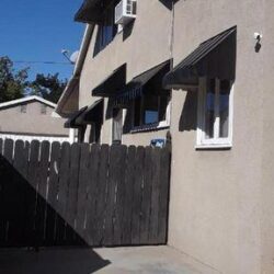 house with black window awnings and brown fence - custom awnings - custom awnings near me - custom awnings for decks - custom awnings for business - custom door awnings near me - spear awnings - aluminum awnings - dome awnings