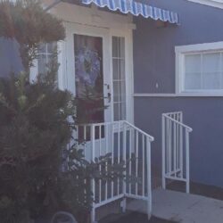 light blue house with blue spear awnings for its white door - custom awnings - custom awnings near me - custom awnings for decks - custom awnings for business - custom door awnings near me - spear awnings - aluminum awnings - dome awnings