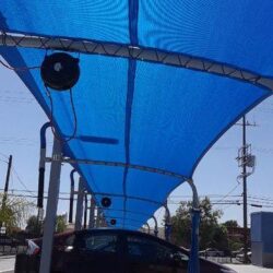 a maroon sedan car under a blue carport during the day - roll ups curtain - custom awnings - concave awnings - window awning design ideas - restaurant awnings - patio awnings - commercial awnings - entrance canopies - privacy fence panels