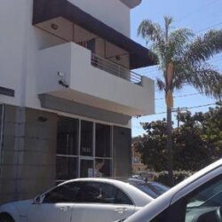a white and grey building with brown awnings for balcony with two white grey cars in front and trees in the background - standard awnings - dome awnings - restaurant awnings - spear awnings - patio enclosures - custom awnings