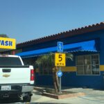 a white car going inside a car wash with blue awnings - custom awnings - custom awnings near me - custom awnings for decks - custom awnings for business - custom door awnings near me - spear awnings - aluminum awnings - dome awnings