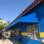 blue store with blue awnings with a lady waiting in front - custom awnings - custom awnings near me - custom awnings for decks - custom awnings for business - custom door awnings near me - spear awnings - aluminum awnings - dome awnings