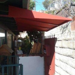 house with red sail shade and red gate - custom awnings - custom awnings near me - custom awnings for decks - custom awnings for business - custom door awnings near me - spear awnings - aluminum awnings - dome awnings