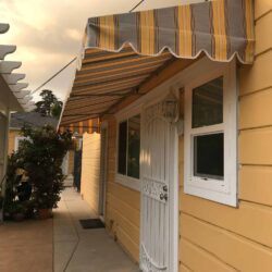 stripe yellow straight awnings for a yellow house with a white entrance door - custom awnings - custom awnings near me - custom awnings for decks - custom awnings for business - custom door awnings near me - spear awnings - aluminum awnings - dome awnings