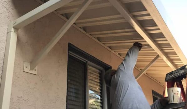 a man on a ladder installing a white aluming awnings for a house - standard awnings - concave awnings - aluminum awnings - carports - store front awnings - patio shades