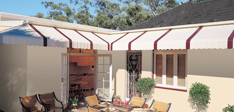 White aluminum patio covers with brown stripes over windows and door in patio with a table and chairs.